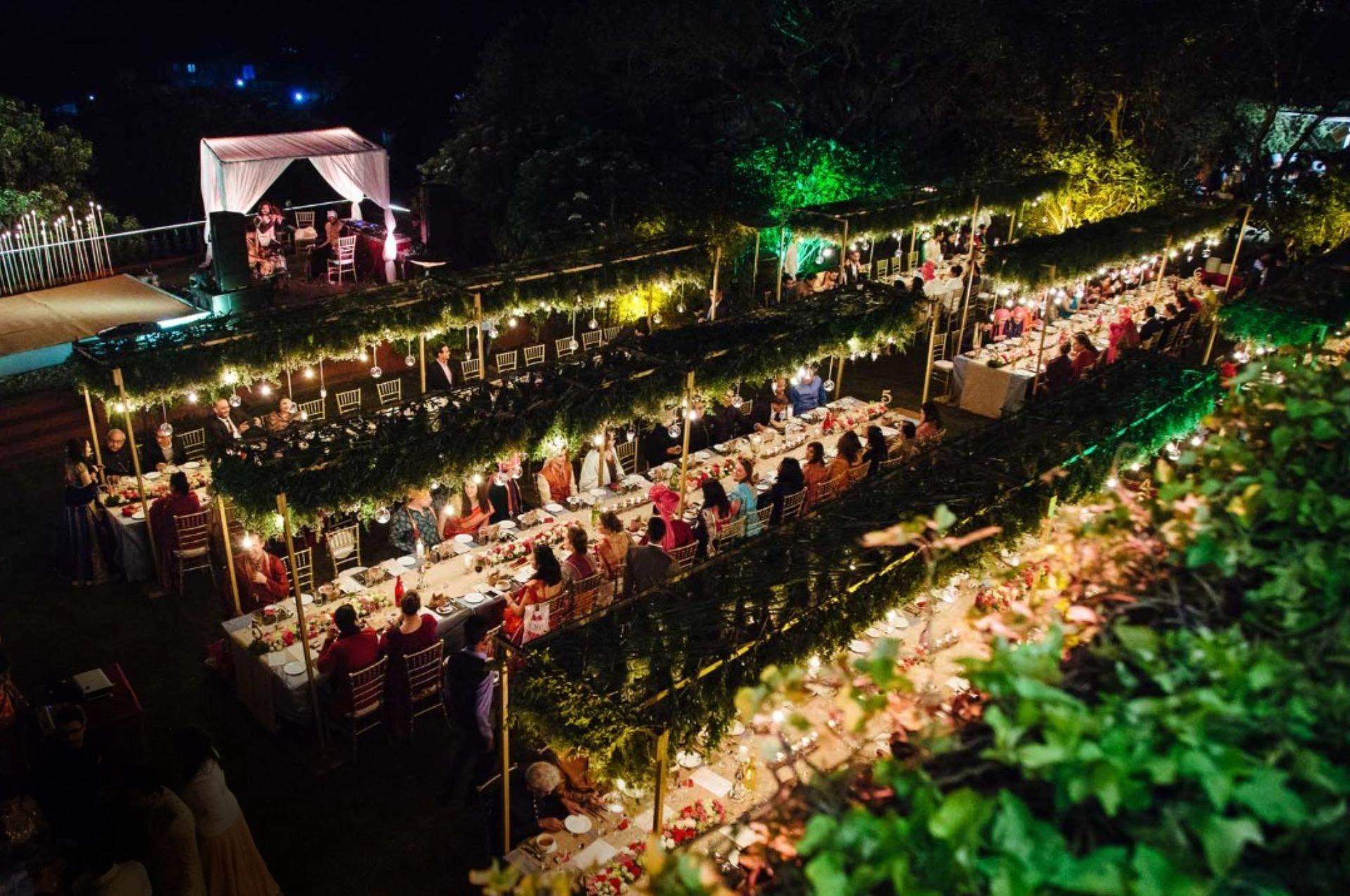 Ramsukh Resort’s lawn with a long sit-down dinner arrangement lit with string lights for a night event.